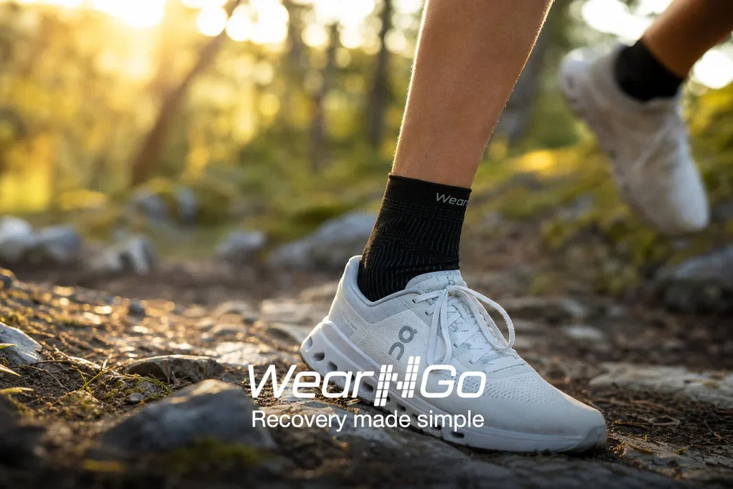Wear'N'Go fotledsstöd på joggare på norsk skogsstig: svart stickad kompressionshylsa med Wear'N'Go-logotypen synlig ovanför löparskor, morgonljus genom träden
