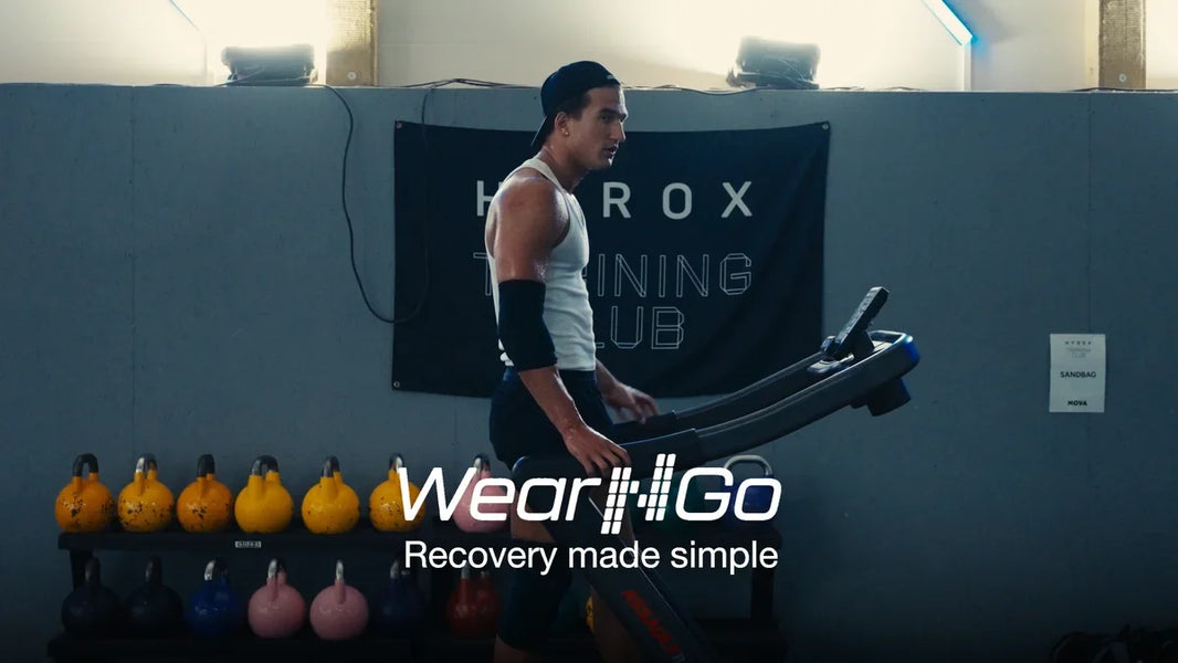 Löpning på löpband framför en HYROX Training Club-vägg i ett gym, med Wear'N'Go kompressionsärm på armen